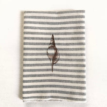 Cargar imagen en el visor de la galería, Servilleta de algodón con rayas azules sobre fondo crudo, con un estilo muy marinero. El bordado es de concha marina realizado con hilo de color marrón
